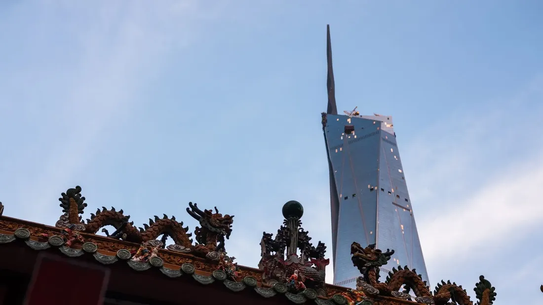 Dragon sculptures on a traditional roof against a blue sky with a modern skyscraper.
