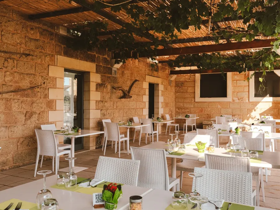 Restaurant extérieur avec tables et chaises blanches, décoration verte, et murs en pierre chez Masseria Stali.