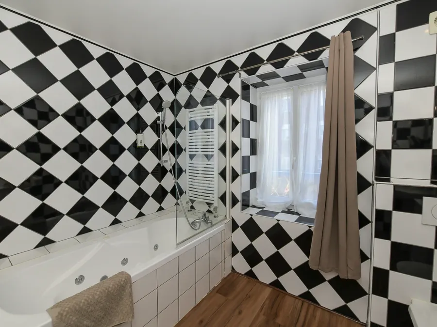 Salle de bain élégante avec carrelage damier noir et blanc, baignoire et fenêtre à l'Hôtel Villa Aultia à Ault.