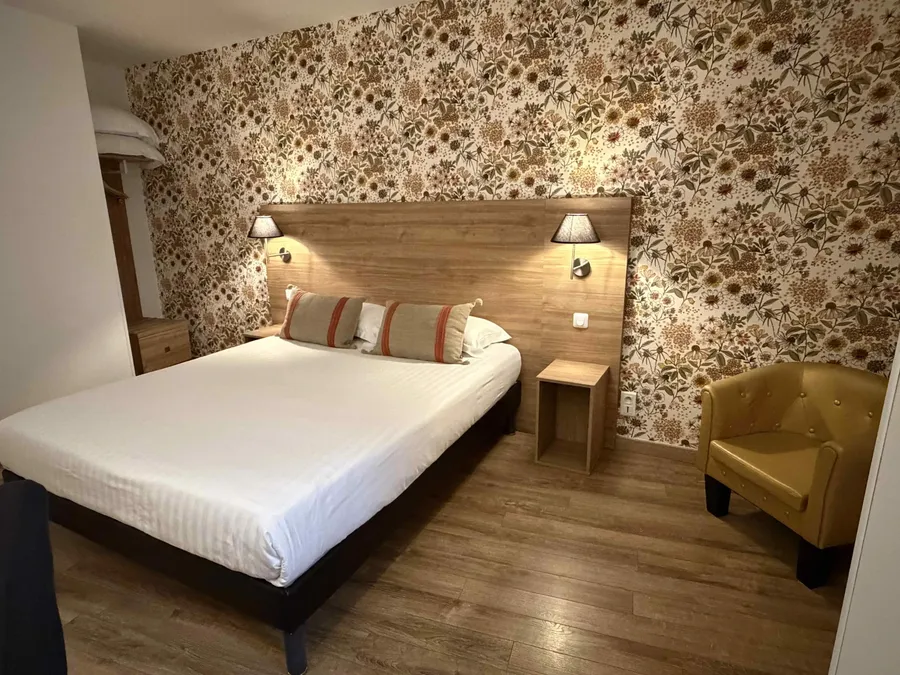 Chambre confort au Grand Hôtel Molière de Pézenas avec lit, chaise et mur floral.