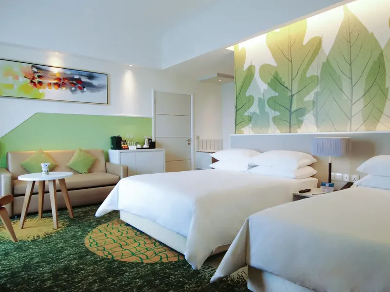 Hotel room with two beds, green and white decor, couch, table, and leaf mural.
