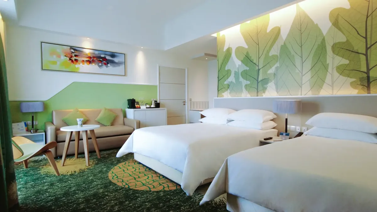 Hotel room with two beds, green and white decor, couch, table, and leaf mural.