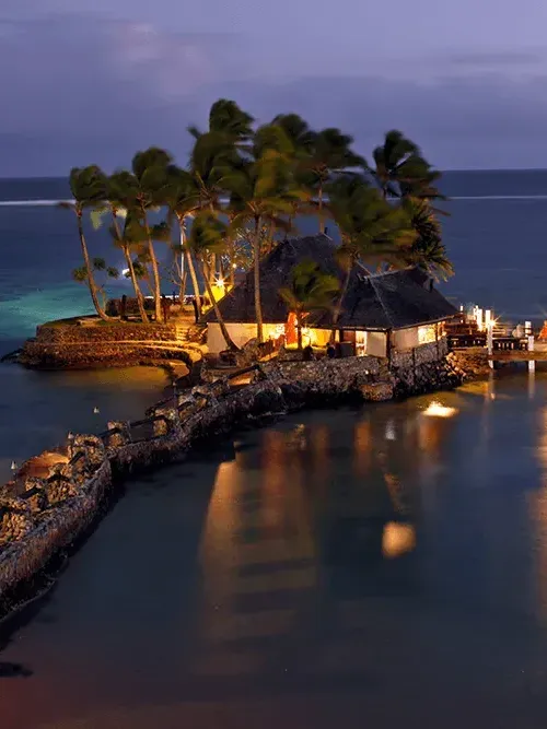 Glowing tropical hut on a private island at twilight with palm trees and calm ocean near Warwick New York