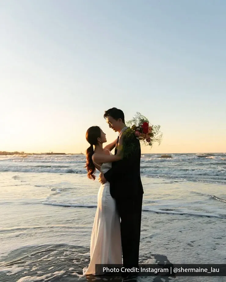 Sea wedding couple posing on beach with bouquet at sunset.