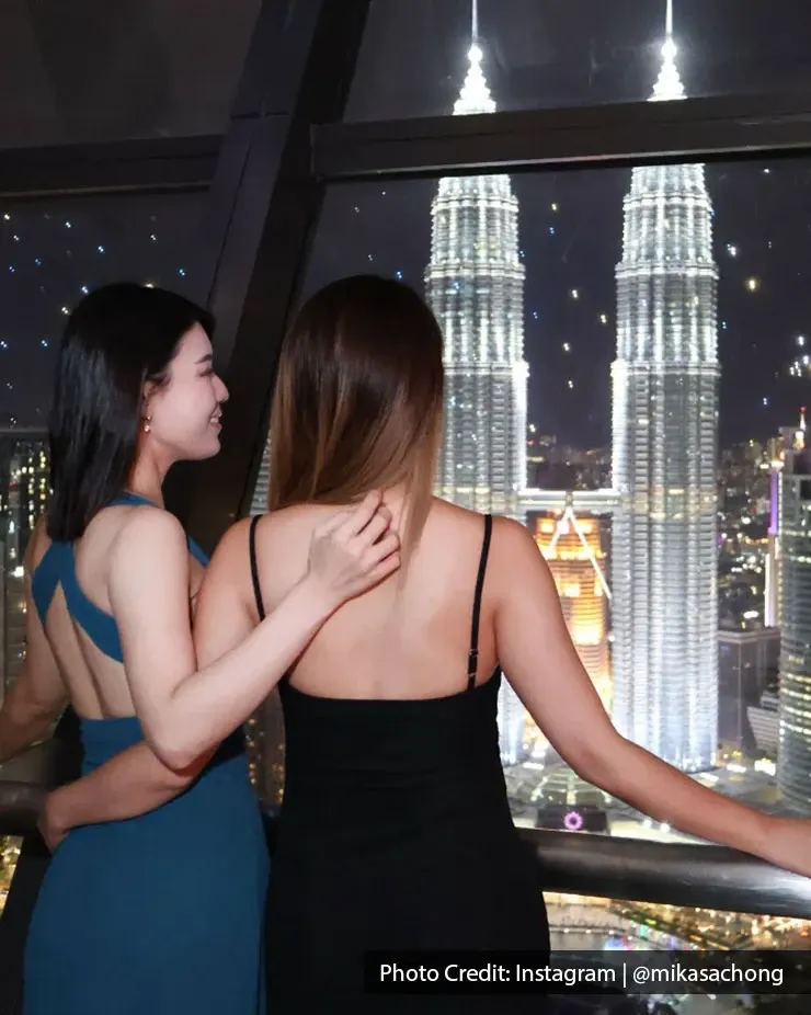 Two woman looking at Petronas Twin Towers during the night.