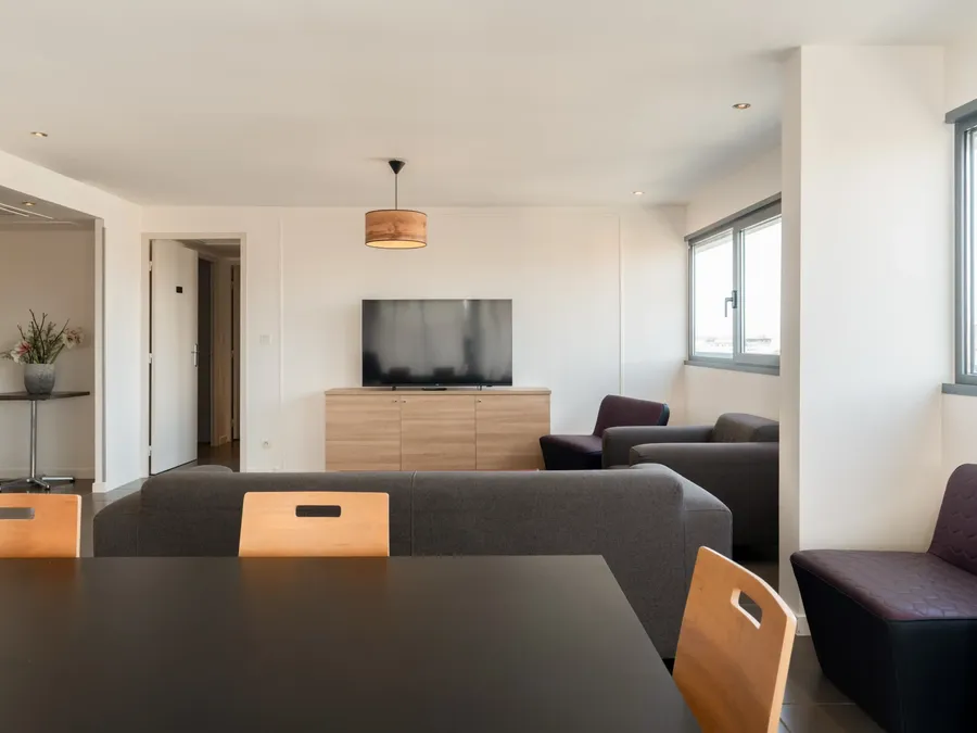 Two-bedroom apartment living area with a TV, couch, and dining table at Appart’Hôtel Hévéa, Valence.