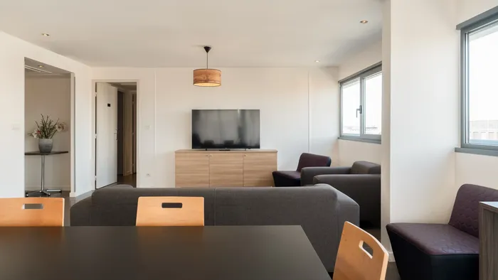 A living room with gray sofa and TV at Appart’Hôtel Hévéa.