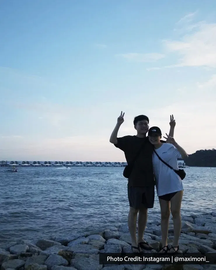 Couple standing on seaside rocks making peace signs at sunset.
