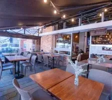 Outdoor restaurant terrace with wooden tables & gray chairs under a roof at Unika Hotels, an elite hotel in Bogota, Colombia