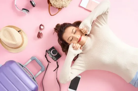A woman smiling and lying on the floor with her travel essentials - Lexis Hotels & Resorts