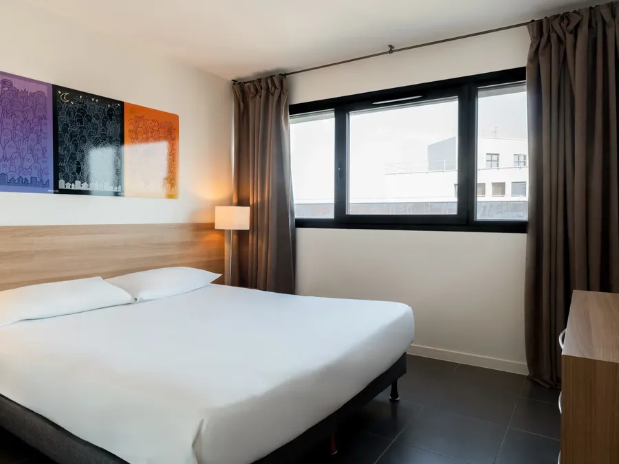 Bedroom with double bed and large window in two-bedroom apartment at Appart’Hôtel Hévéa in Valence.