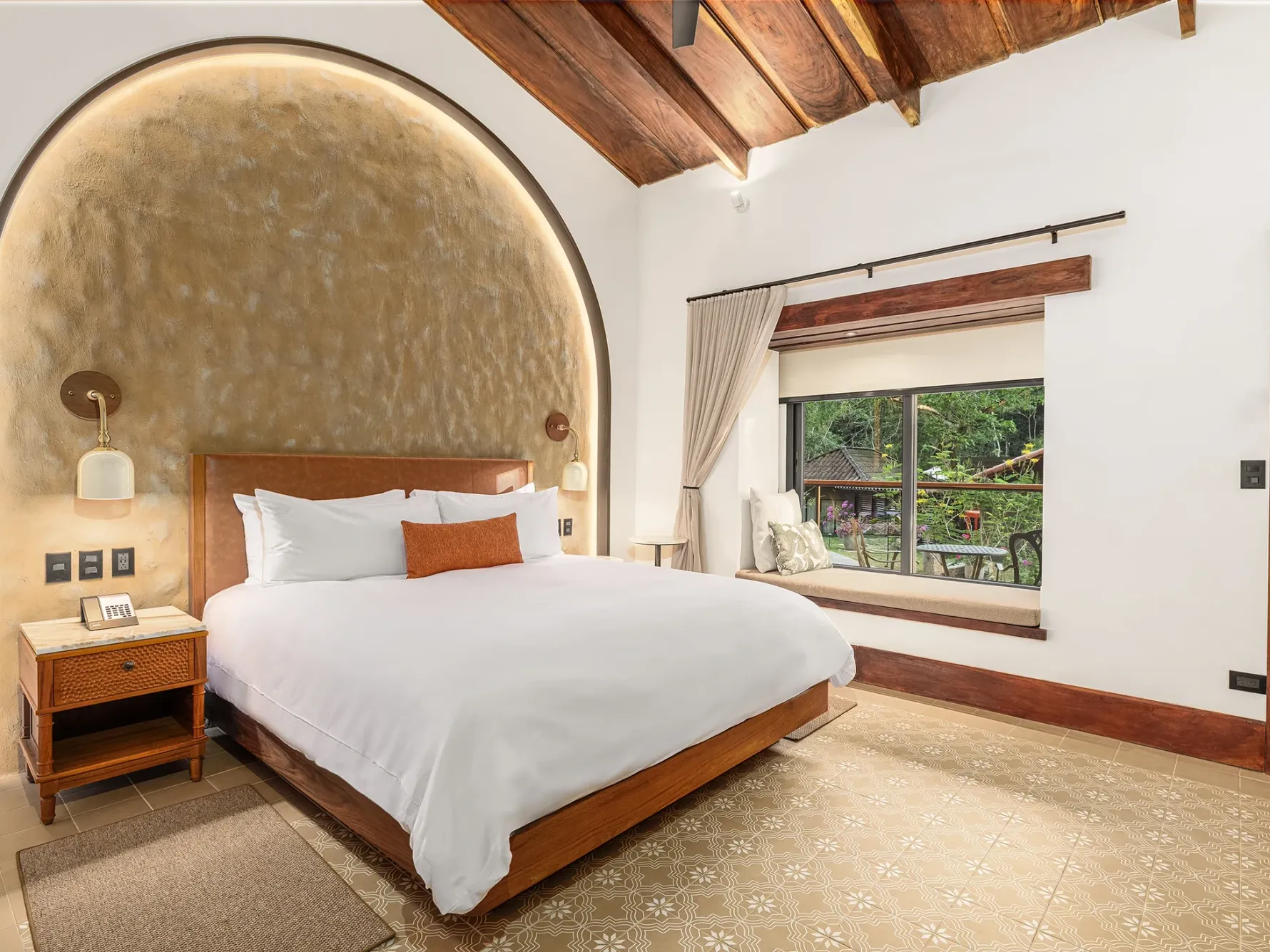Cama situada entre las mesitas auxiliares junto a la ventana en la habitación Deluxe King de la Hacienda Santa Lucía Jungle, uno de los mejores hoteles de Costa Rica