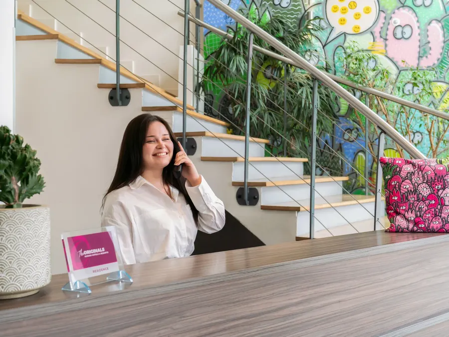 Woman smiling and talking on the phone at the residence reception desk of Appart’Hôtel Hévéa.
