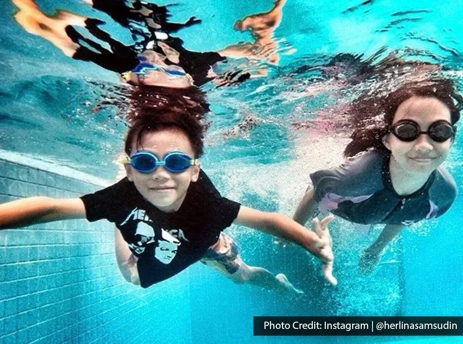 Two people swimming underwater in pool with goggles.