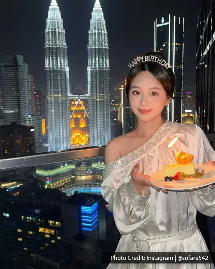 A woman holding her birthday cake in front of the Petronas Twin Towers in Kuala Lumpur.
