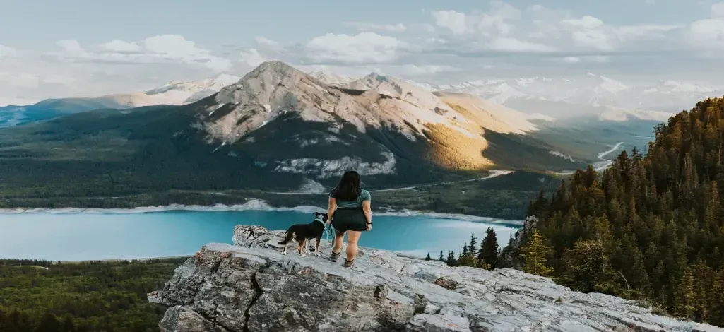 A person and their dog pose at a viewpoint of a mountain near Canmore.