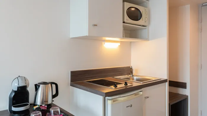 Compact kitchen with microwave, mini fridge, and coffee maker at Appart’Hôtel Hévéa.