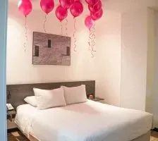 Plush double bed decorated with floating pink balloons against a sleek headboard inside a romantic suite at Unika Hotels