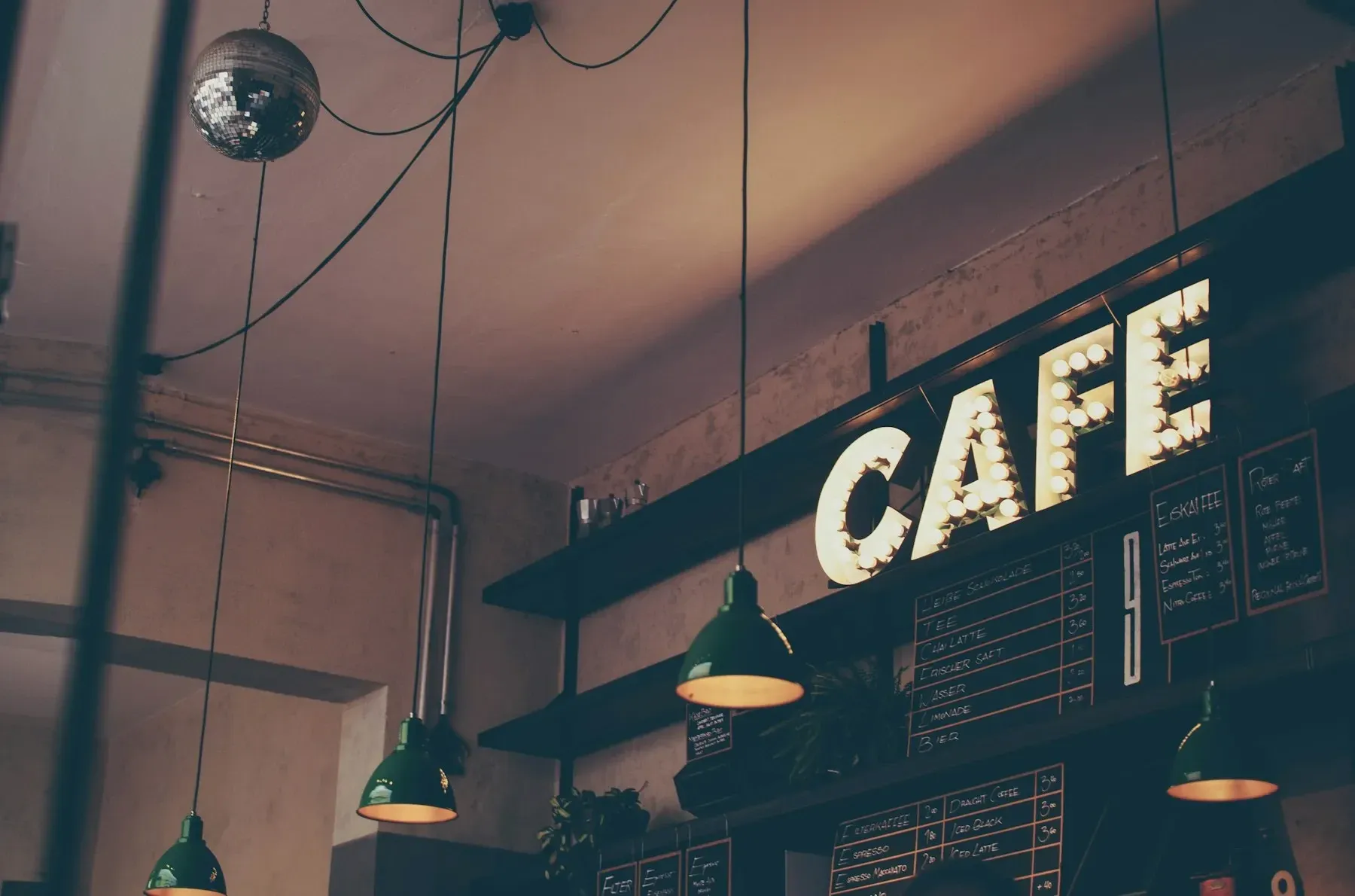 A caf&eacute; interior with a glowing marquee sign and green pendant lamps