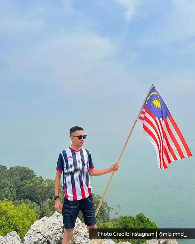 Seorang lelaki memegang bendera Malaysia di atas bukit menghadap laut - Lexis Hibiscus Port Dickson