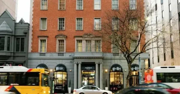 tall brick building showing the facade of The Chancellor on Currie, with cars and a bus passing in front, and a bare tree on the right of the building
