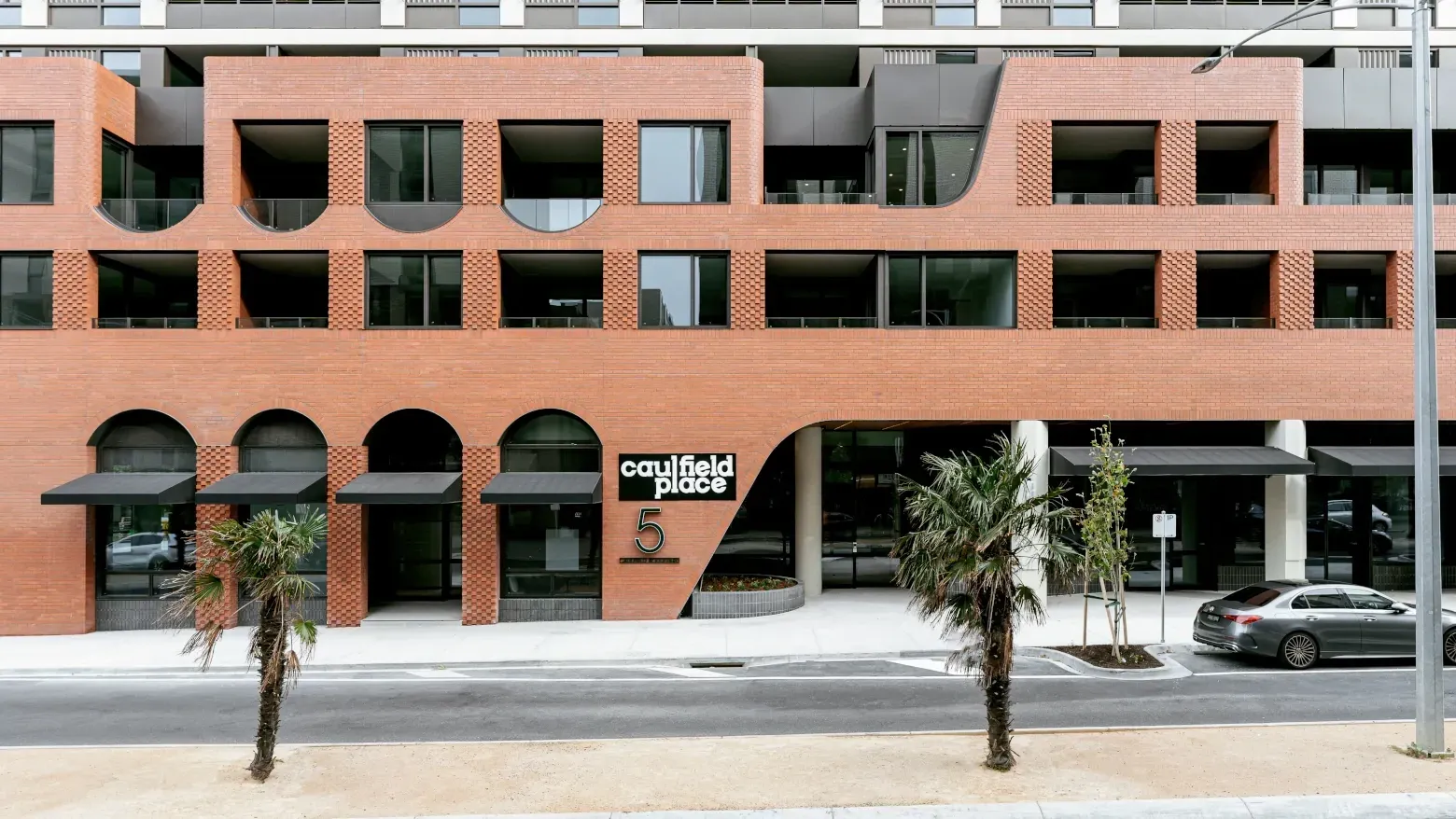 Caulfield Place building exterior with palm trees and a parked car.