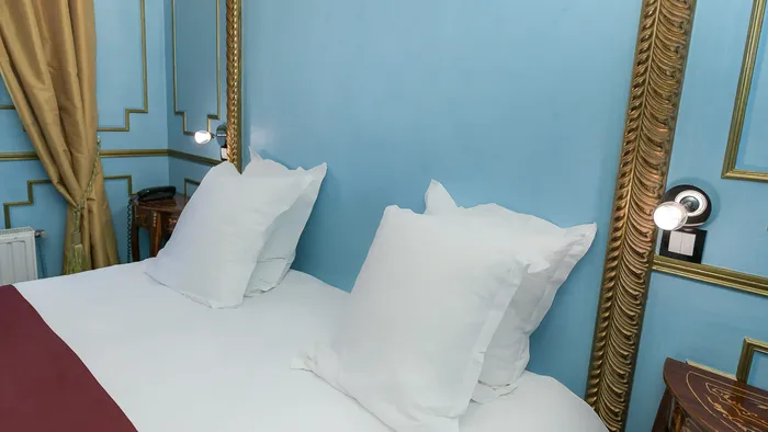 Chambre élégante avec lit et oreillers blancs, murs bleus et cadre doré à l'Hôtel Villa Aultia.