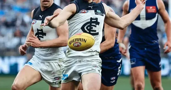 Australian rules football player kicking the ball during a match, with teammates and opponents running behind him on the field.