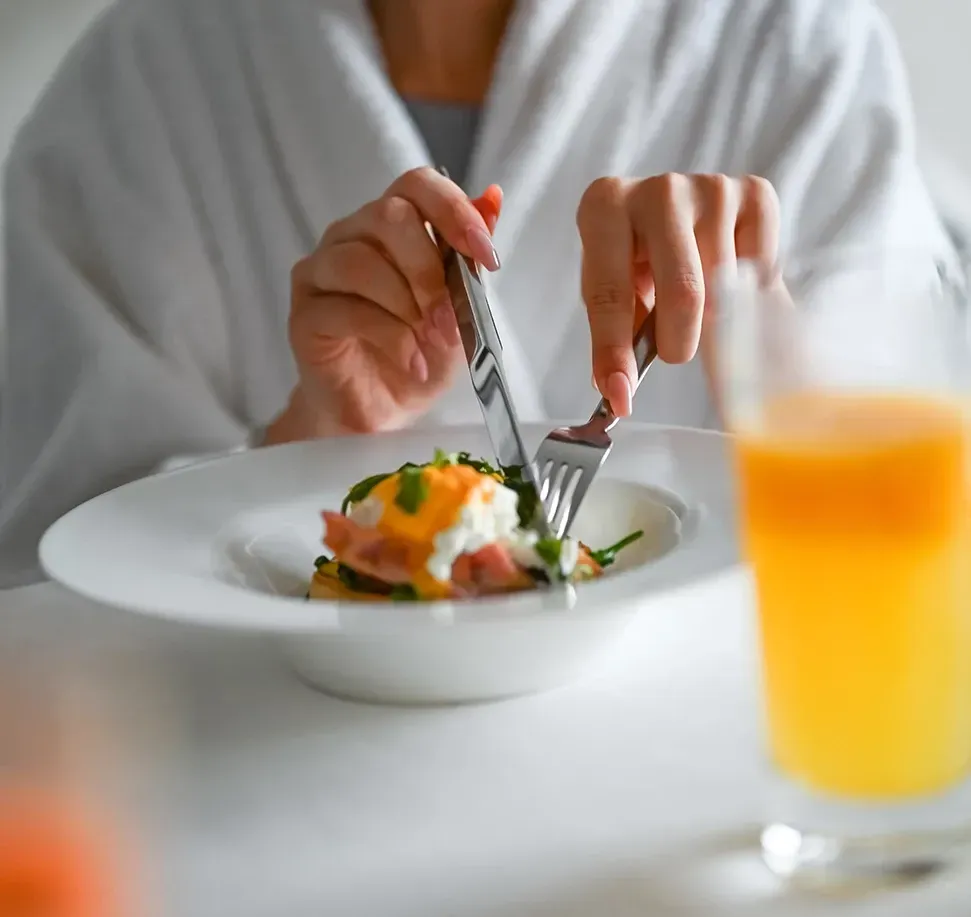 A person in a white robe cutting food on a plate with a knife and fork.