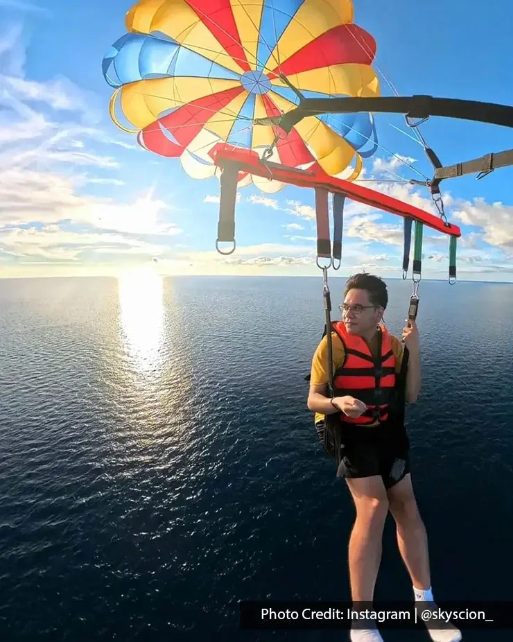 Person parasailing over ocean beneath colourful parachute.