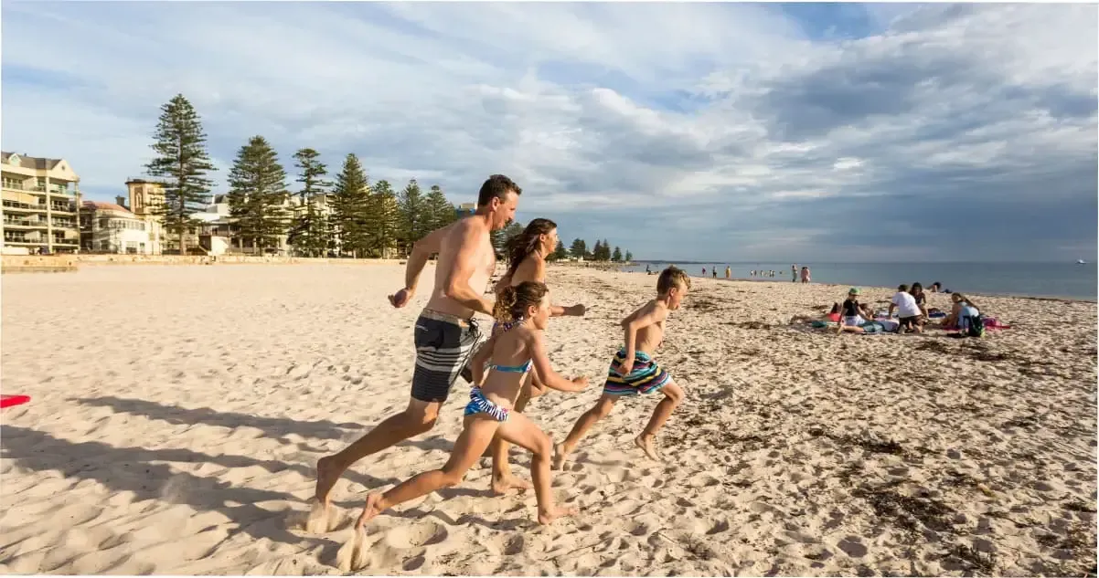 A family runs on the sand towards the water at Glenelg Beach