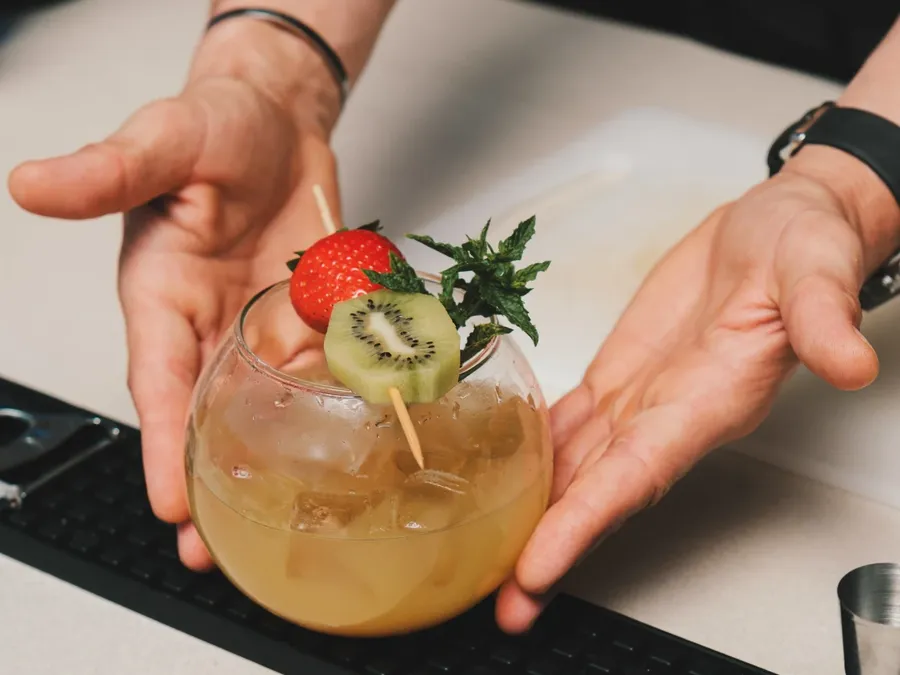 Personne tenant un cocktail décoré avec une fraise et une tranche de kiwi à Masseria Stali.