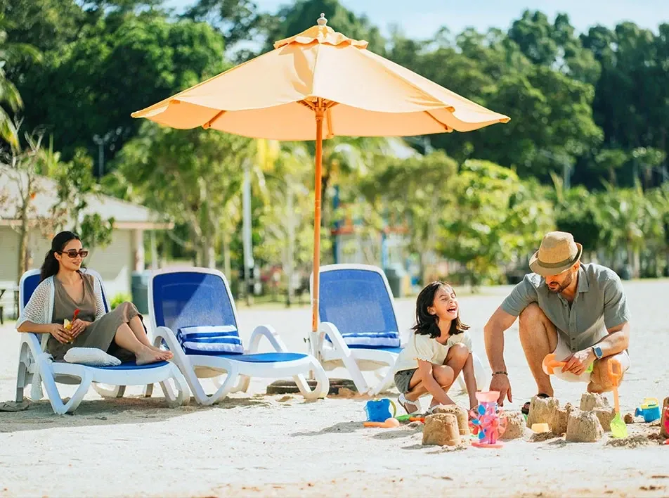 Family enjoying a sunny beach day while building sandcastles under a beach umbrella.