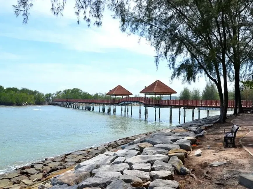 A scenic pier featuring a wooden bridge leading to a sandy beach under a clear blue sky - Lexis Port Dickson