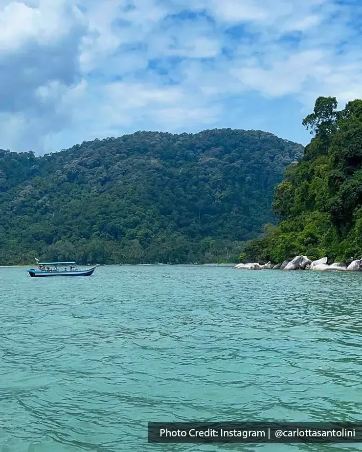 A small boat on a calm lake surrounded by trees at Penang National Park - Lexis Suites Penang