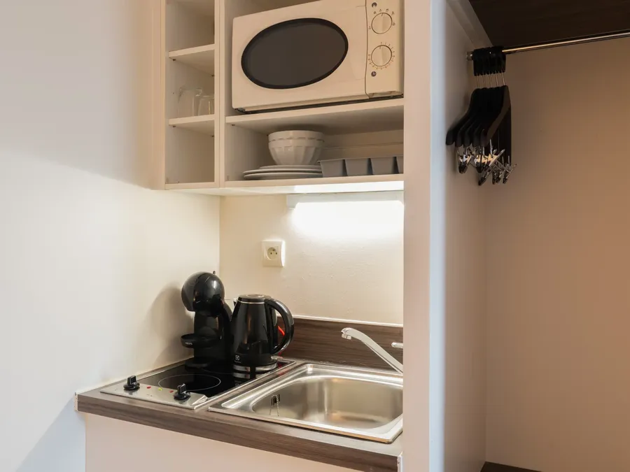 Compact kitchen area with microwave, coffee machine, and sink in a Standard Studio at Appart’Hôtel Hévéa, Valence.