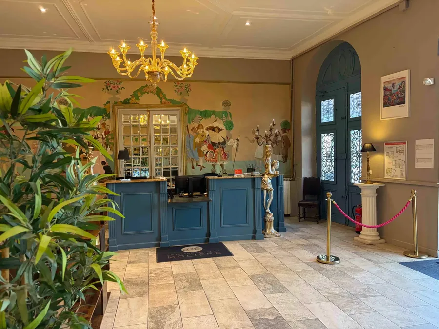Entrée élégante du Grand Hôtel Molière avec réception, lustre, et plantes vertes.