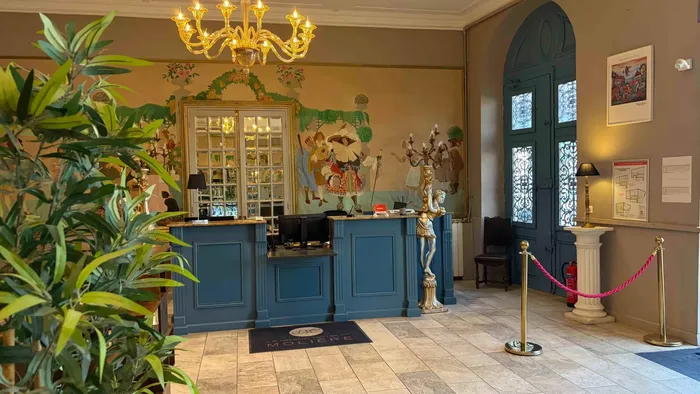 Entrée élégante du Grand Hôtel Molière avec réception, lustre, et plantes vertes.