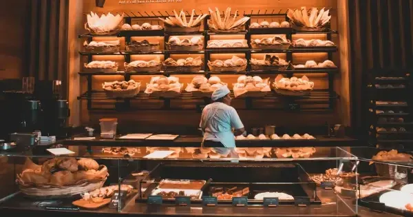 A barista prepares fresh bread and pastries in a bakery lined with shelves of loaves and croissants