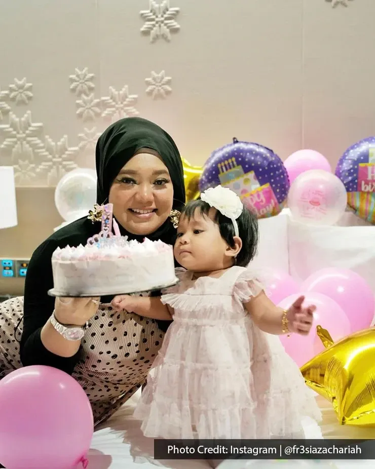 A mother holding a birthday cake and posing for a birthday photo with her daughter in a hotel room.