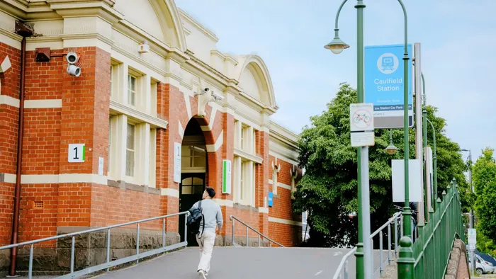 Pedestrian walking towards Caulfield Station with signs and green railing.