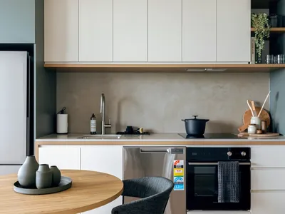 Modern kitchen with white cabinets, black appliances, and wooden table at Caulfield Place.