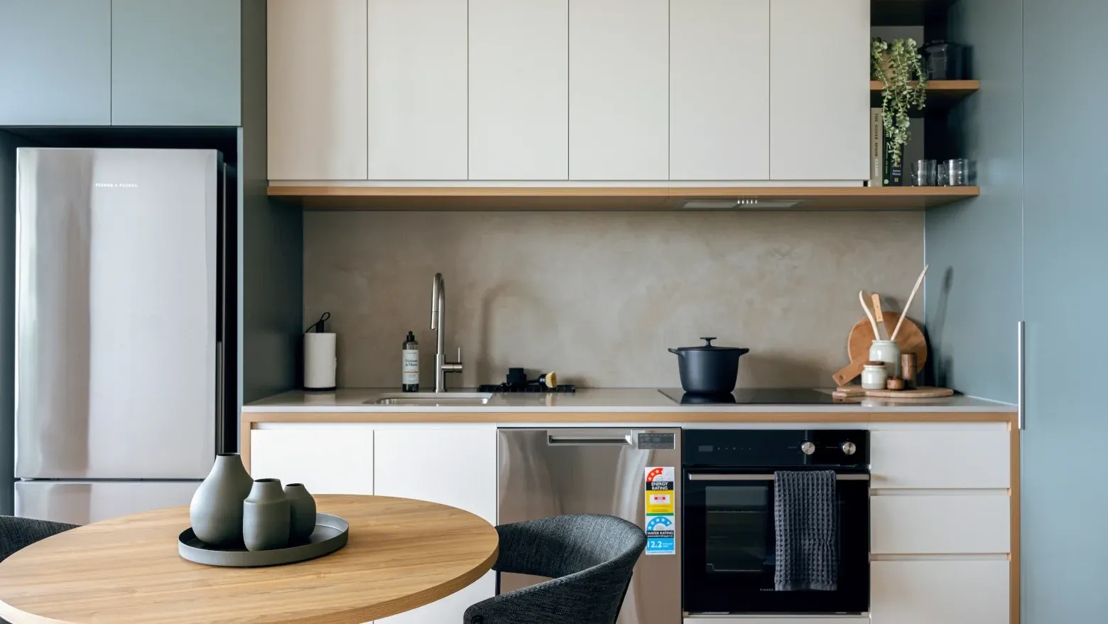 Modern kitchen with white cabinets, black appliances, and wooden table at Caulfield Place.
