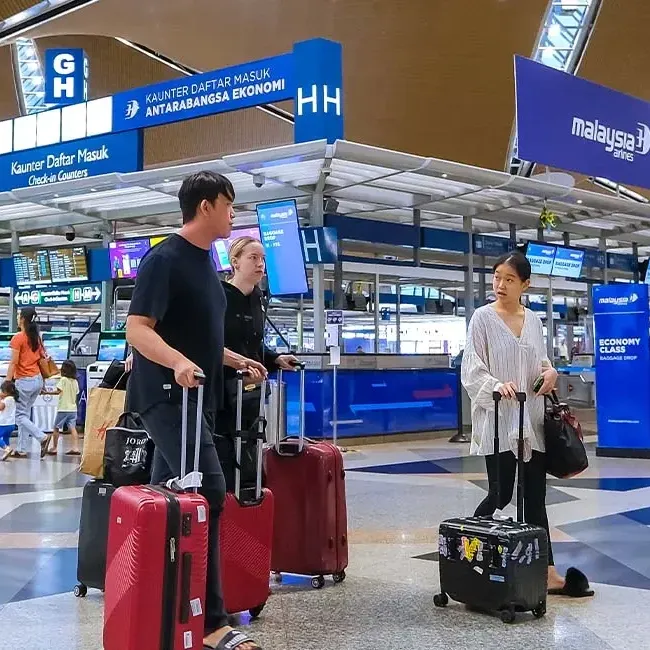 A group of travellers stands in an airport terminal while holding their luggage - Lexis Hotel Group