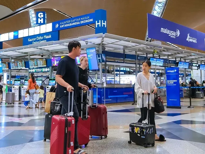 A group of travellers stands in an airport terminal while holding their luggage - Lexis Hotel Group