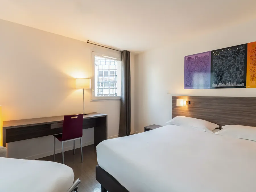 Quadruple studio with white bedding and artwork at Appart’Hôtel Hévéa in Valence.