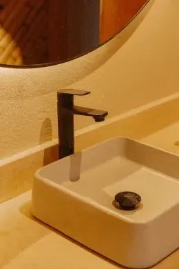 Round mirror mounted above a black faucet, with a square white basin resting on a smooth marble vanity at Unika Hotels