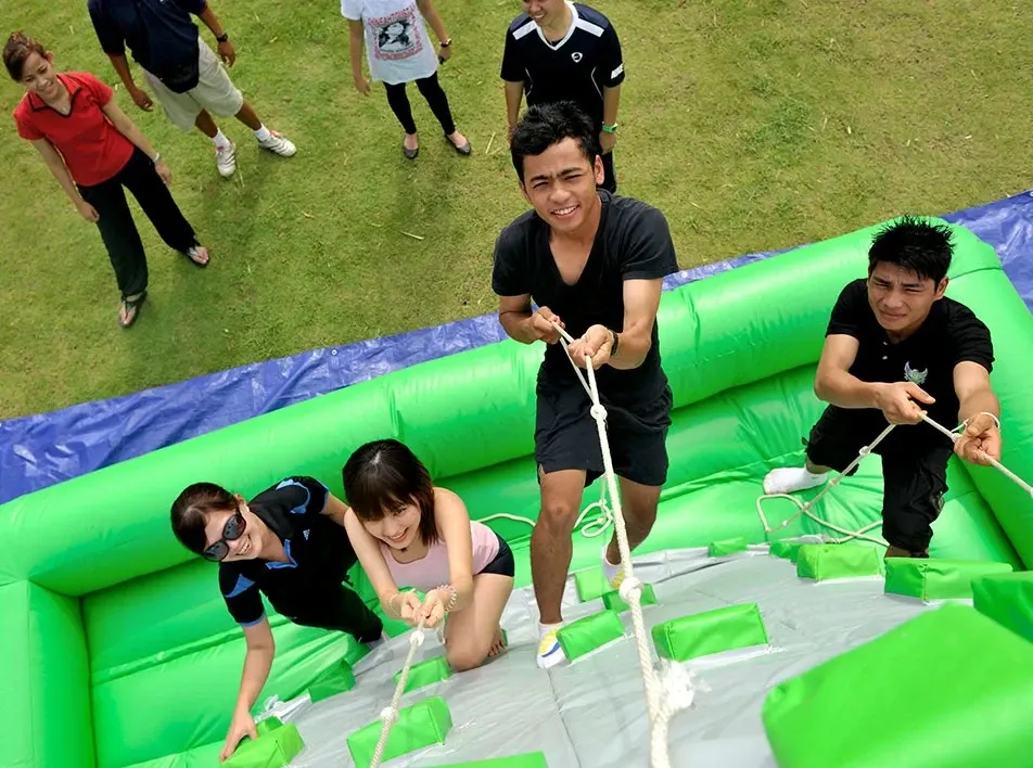 Team building games with participants climbing inflatable obstacle using ropes.