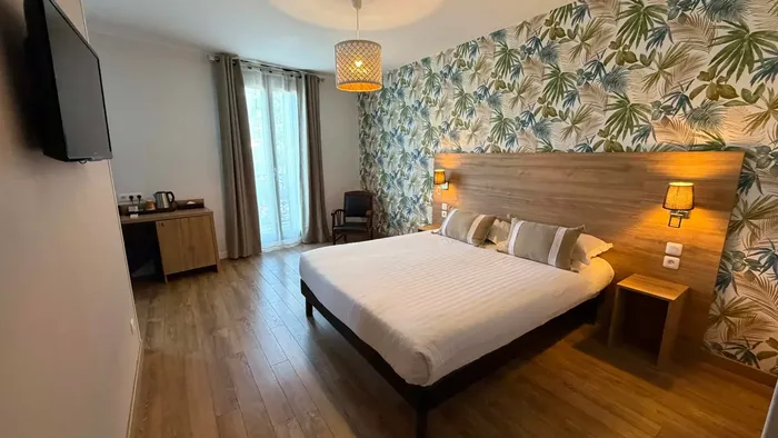 Chambre moderne avec lit, bureau, télévision et mur tropical au Grand Hôtel Molière.