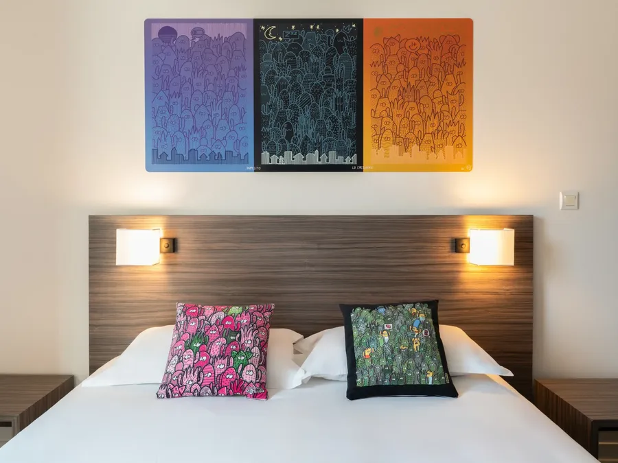 A bedroom with a bed, pillows, and a wall painting at Appart’Hôtel Hévéa.